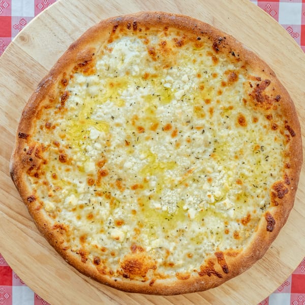 White pizza with ricotta, mozzarella, olive oil, and herbs on a wooden peel over a red and white tablecloth.