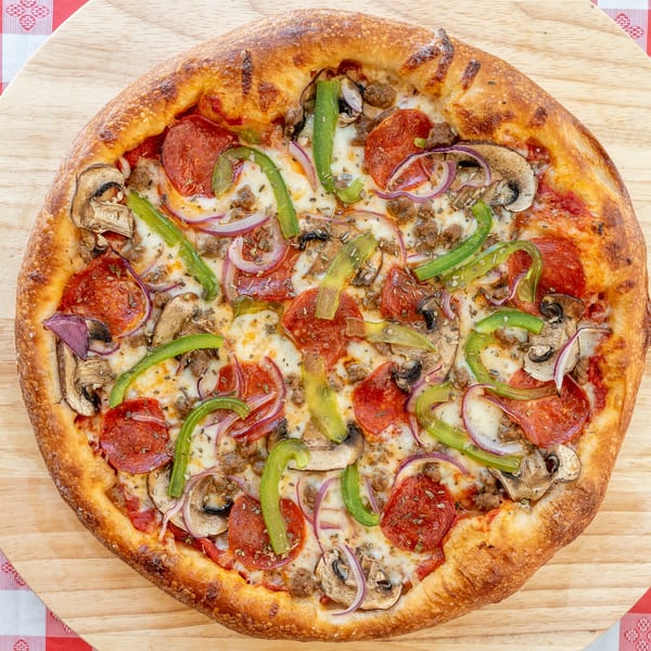 A whole pizza with pepperoni, sausage, mushrooms, green peppers, and red onions on a wooden board.