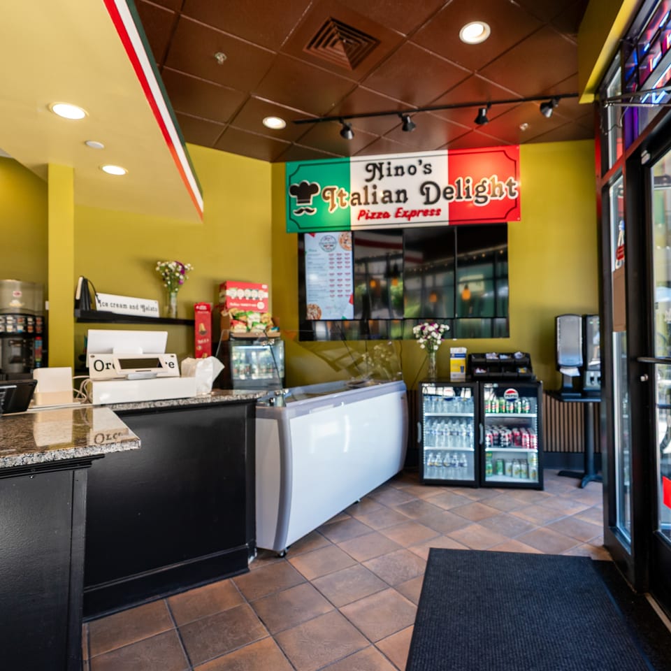 Interior of Nino's Italian Delight Pizza Express, showing the counter, menu board, and drink coolers.