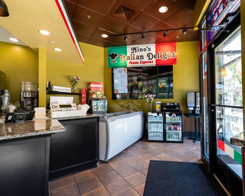 Interior of Nino's Italian Delight Pizza Express, showing the counter, menu board, and drink coolers.