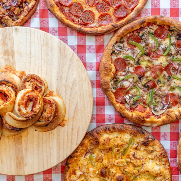 Assortment of pizzas and pepperoni rolls on a red and white checkered tablecloth.