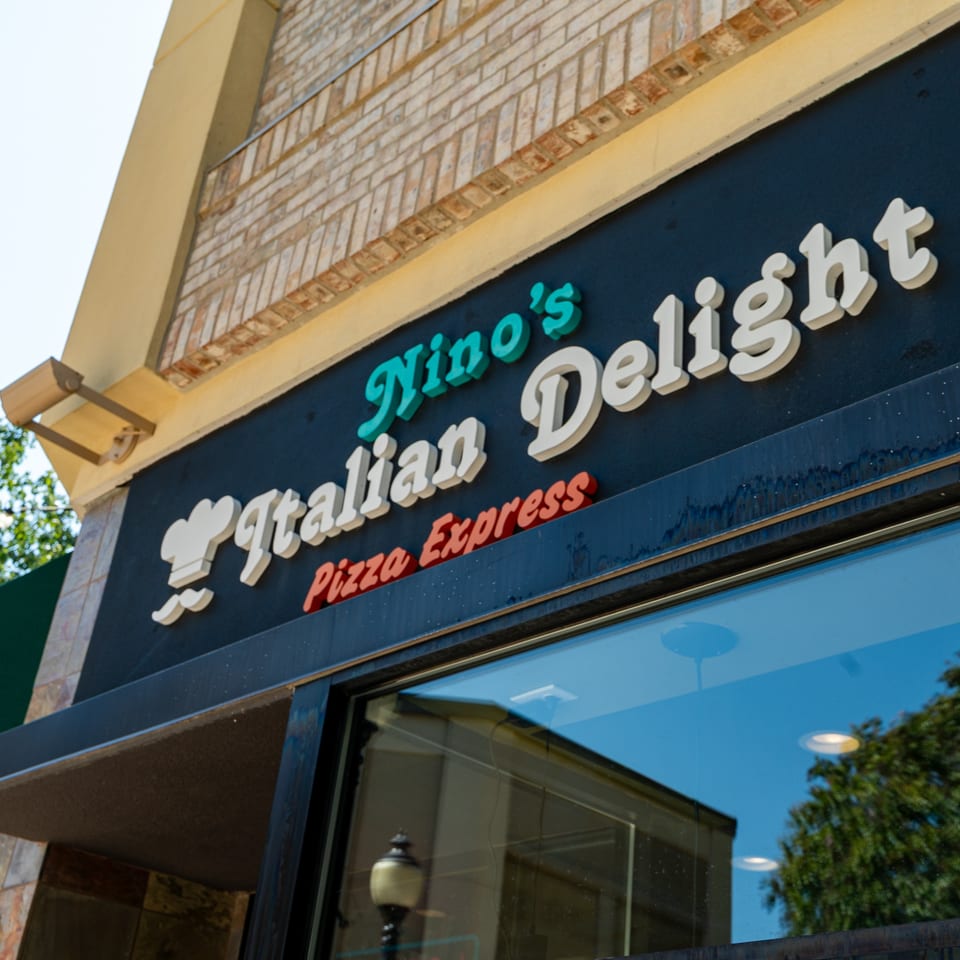 Exterior view of Nino's Italian Delight Pizza Express sign on a black facade with brick above.