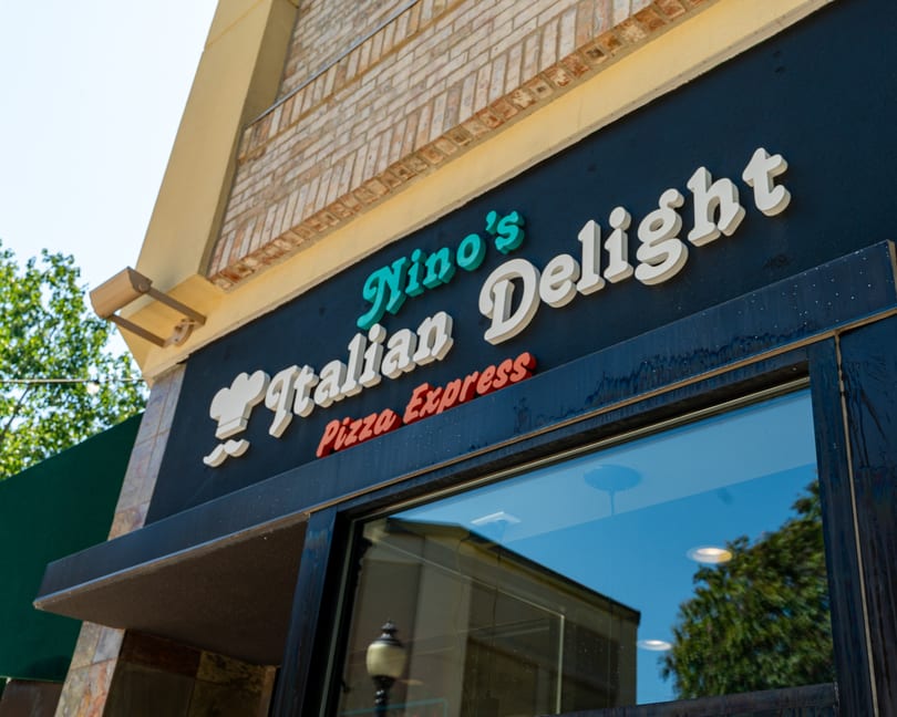 Exterior view of Nino's Italian Delight Pizza Express sign on a black facade with brick above.