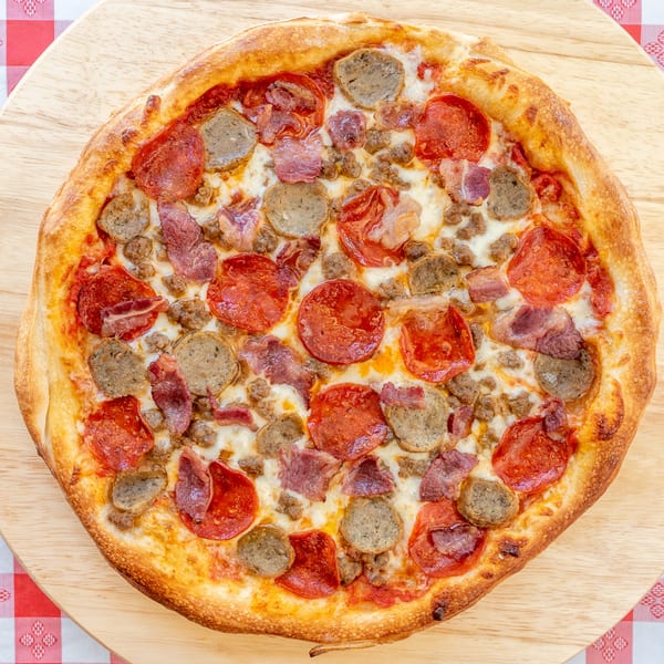 A freshly baked meat lover's pizza with pepperoni, sausage, and bacon on a wooden board.