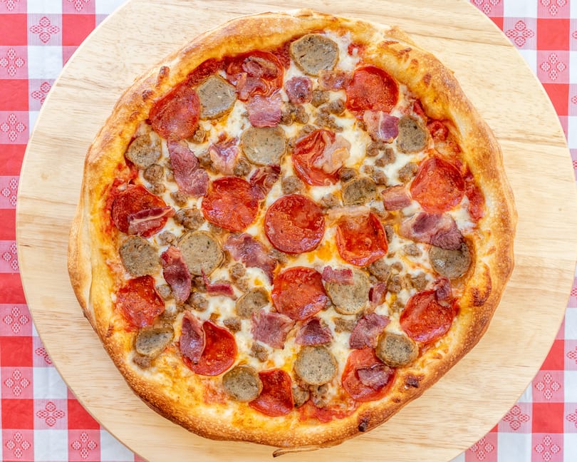 A freshly baked meat lover's pizza with pepperoni, sausage, and bacon on a wooden board.