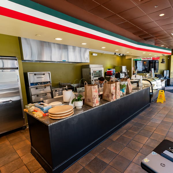 Interior of a Pizza Express restaurant with a counter, kitchen equipment, and a person working.