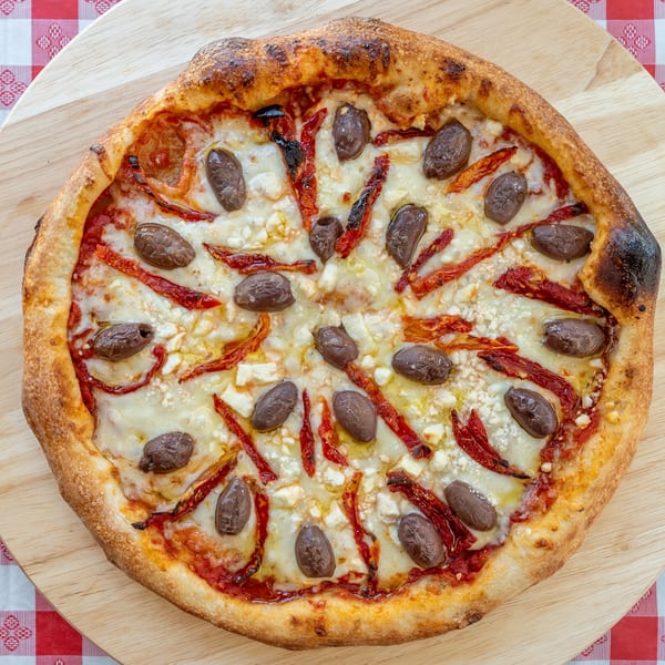 A whole pizza with olives, sun-dried tomatoes, and feta cheese on a wooden board.