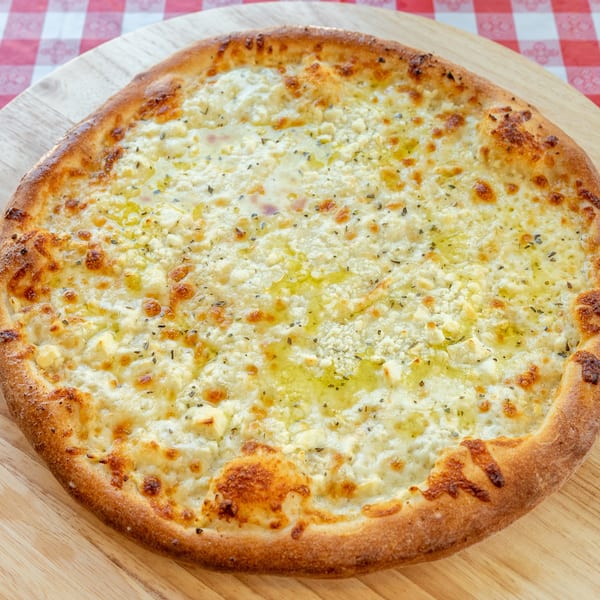 A white pizza with melted cheese, herbs, and olive oil on a wooden peel over a red and white checkered tablecloth.