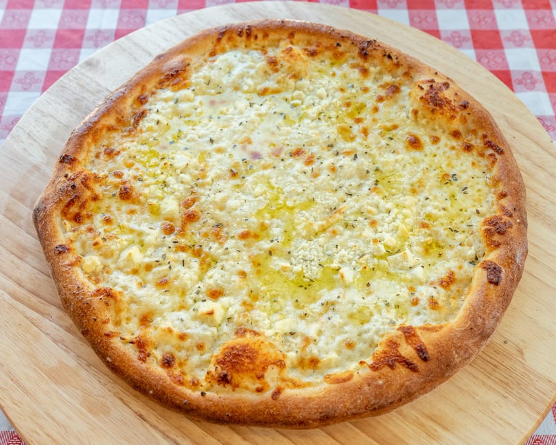 A white pizza with melted cheese, herbs, and olive oil on a wooden peel over a red and white checkered tablecloth.